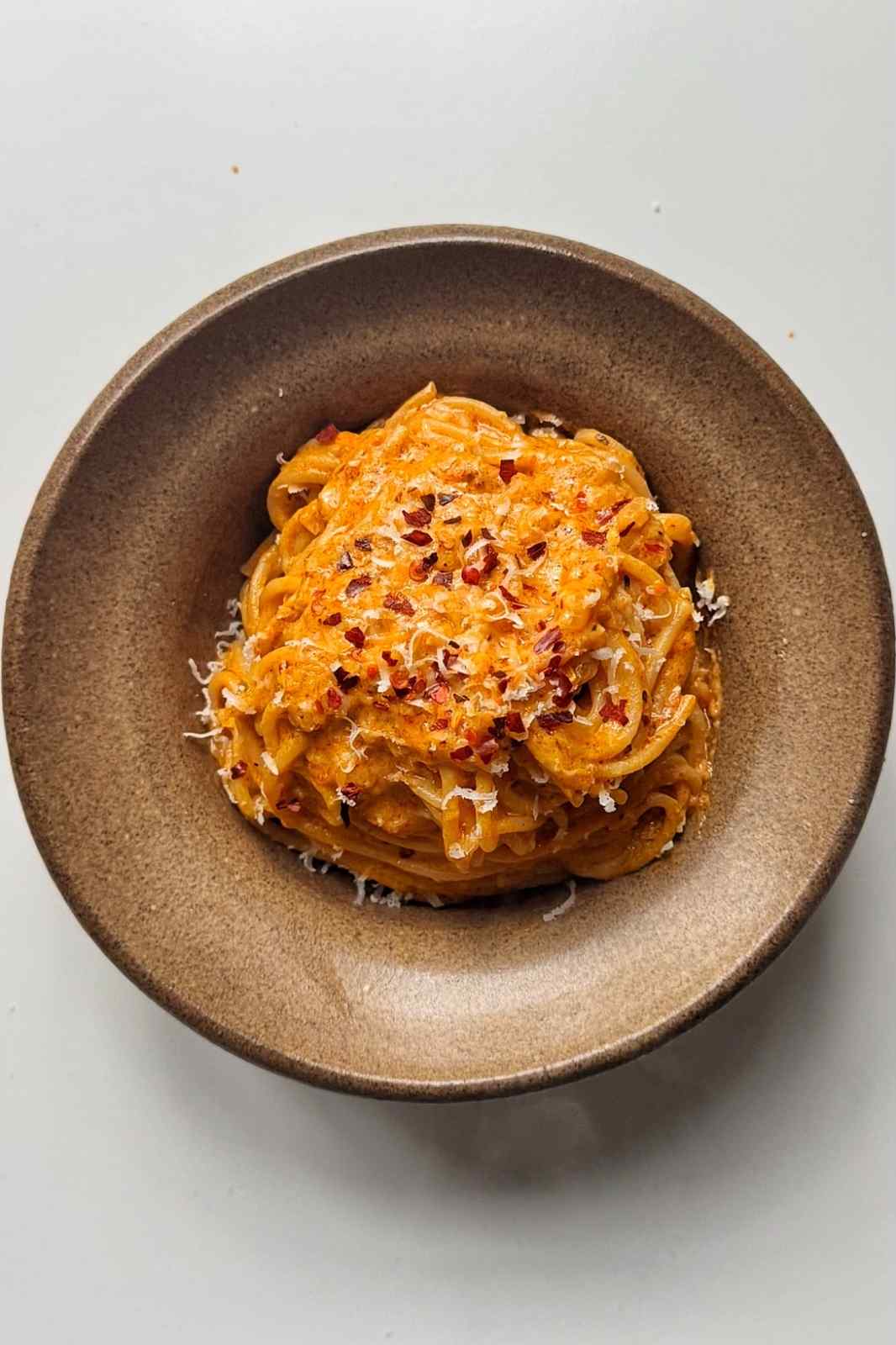 Spicy Boursin pasta with spaghetti in a creamy orange sauce, topped with grated Parmesan and chili flakes, in a brown bowl.