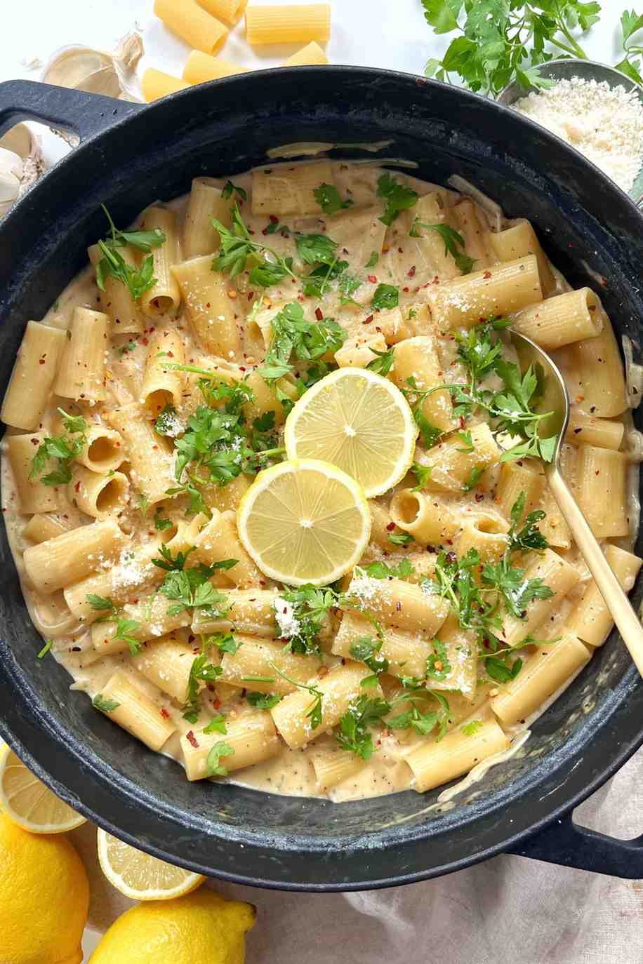 Creamy lemon Boursin pasta with rigatoni in a black pan, topped with parsley, chili flakes, Parmesan and lemon slices.
