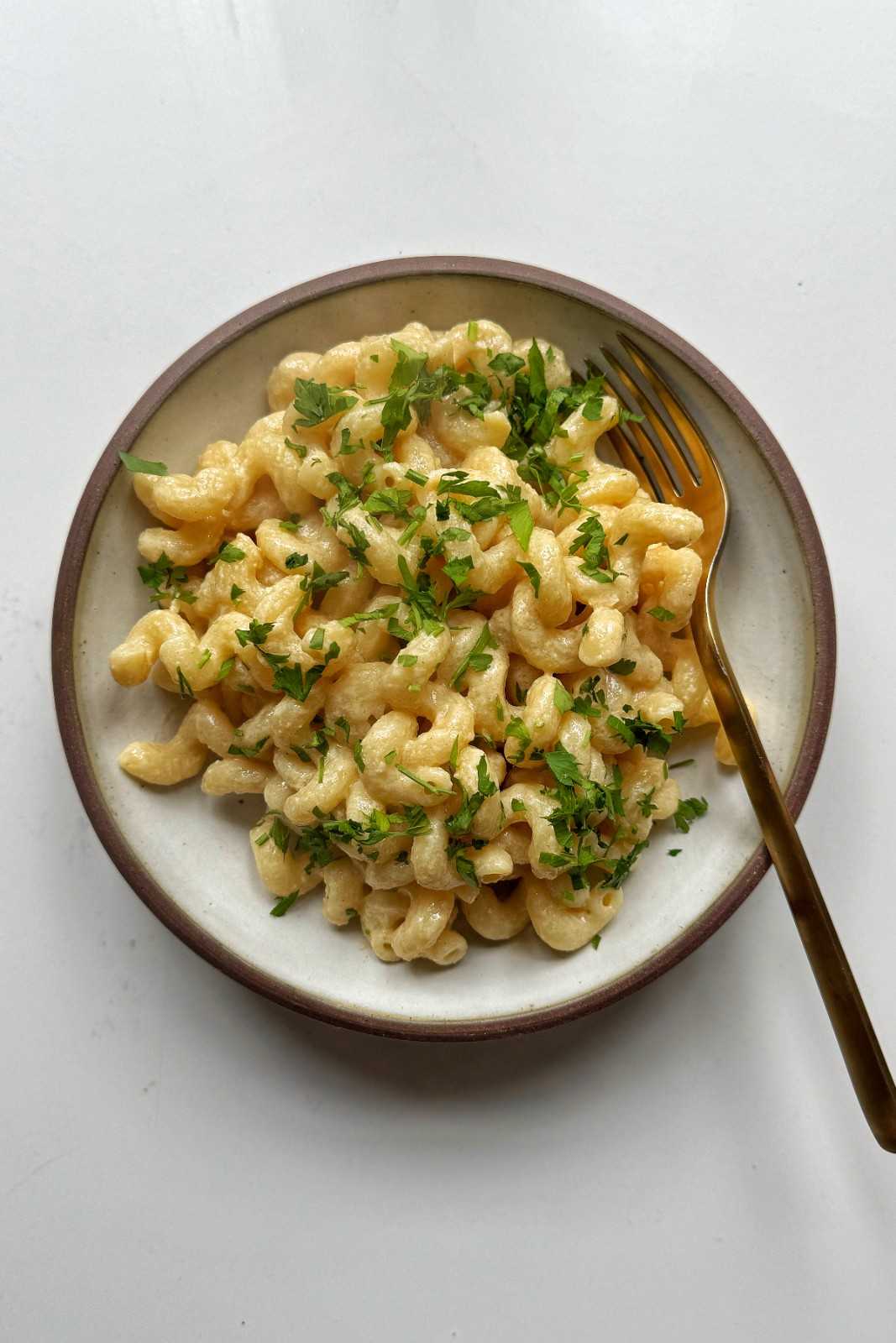 Creamy, dairy-free tahini pasta made with spirali pasta and topped with fresh chopped parsley in a shallow ceramic bowl.