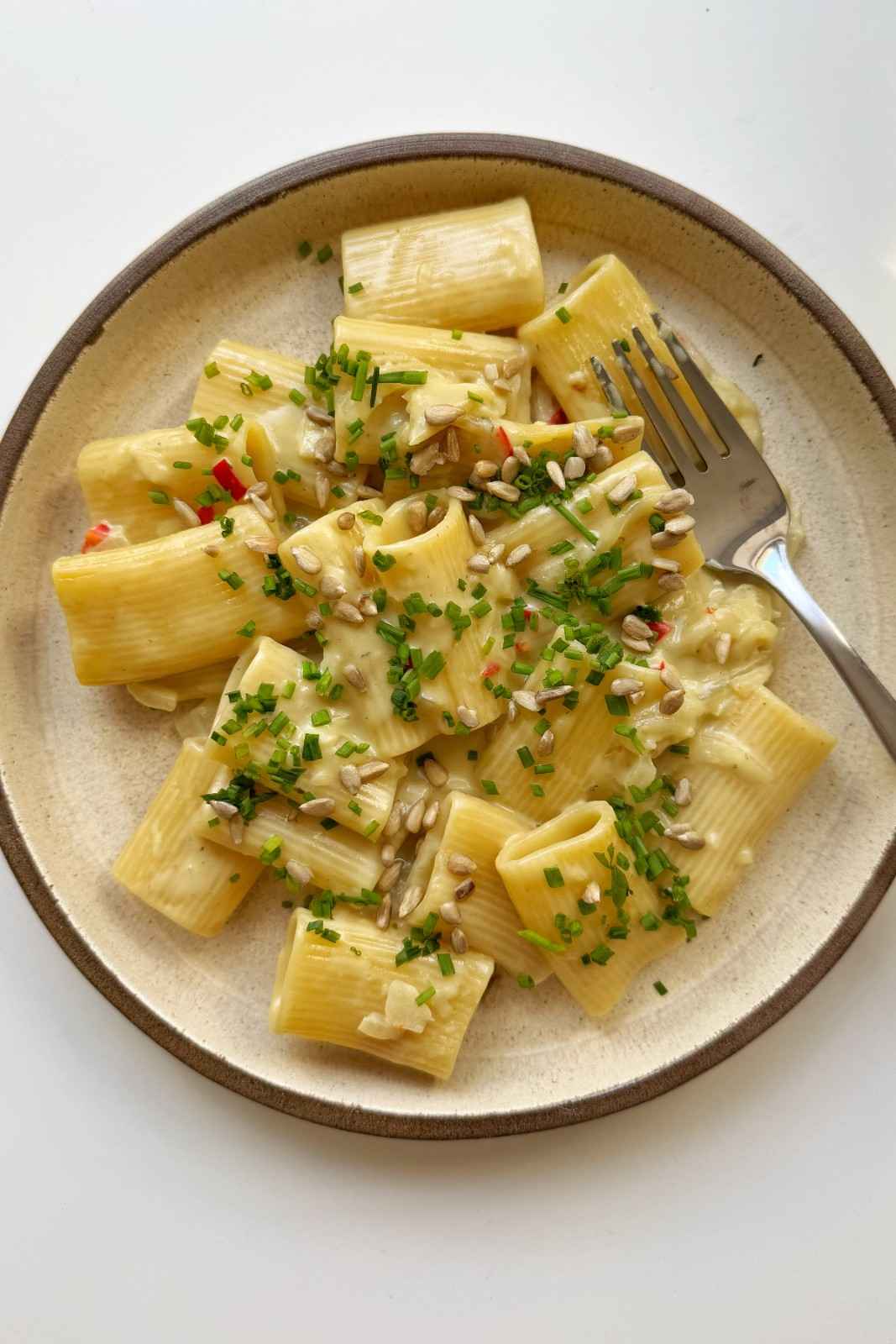 Creamy gorgonzola pasta with rigatoni, topped with chopped chives and sunflower seeds, and hot honey, on a rustic cream plate.