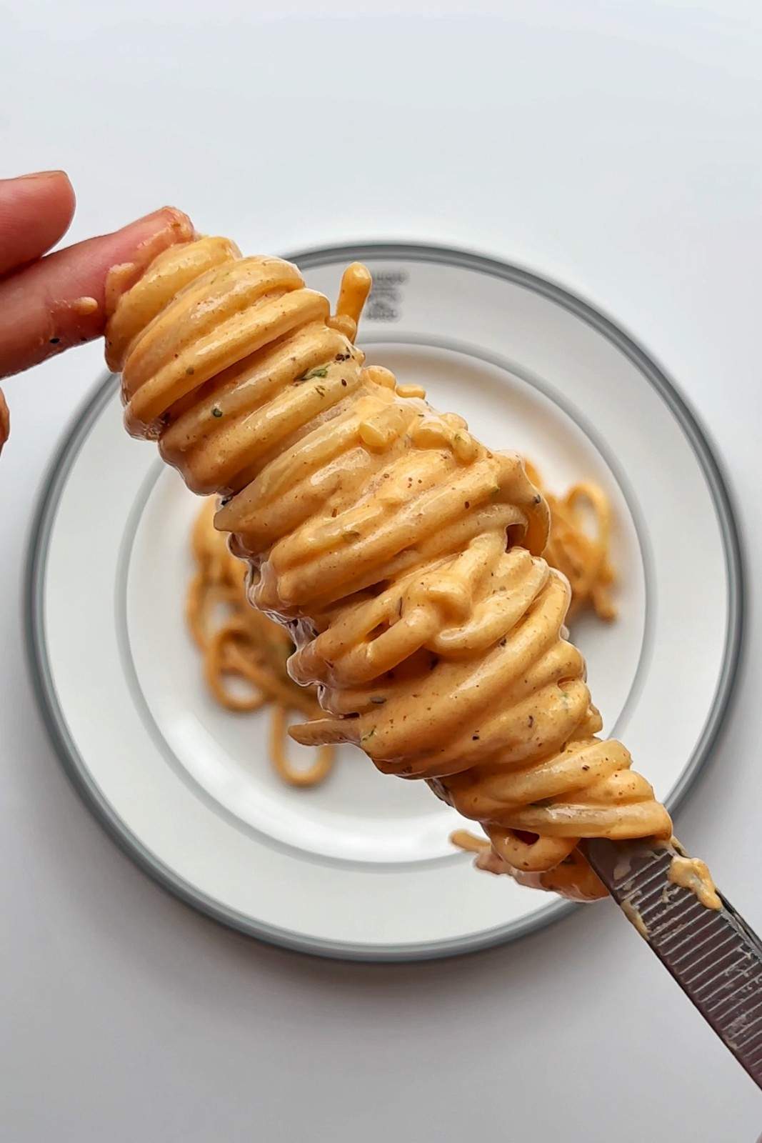 Forkful of creamy spicy gochujang alfredo spaghetti lifted from a plate, coated in a glossy orange creamy sauce.