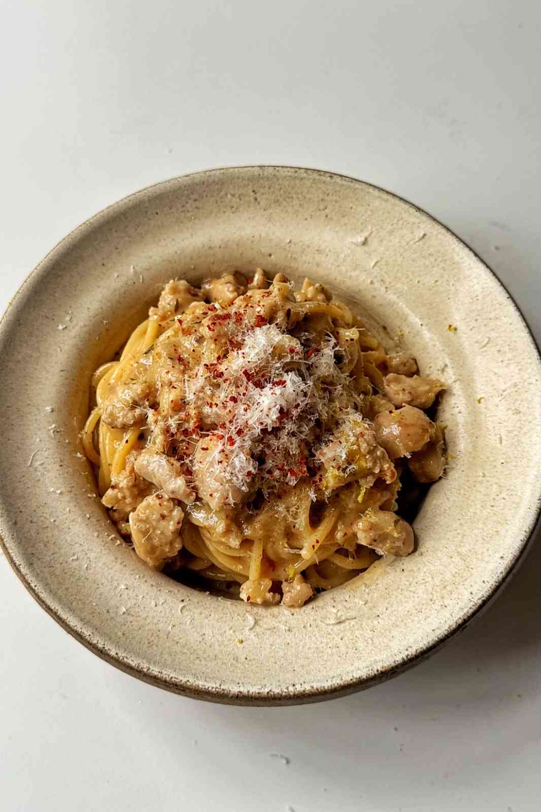 Creamy sausage pasta in cream bowl on white background.