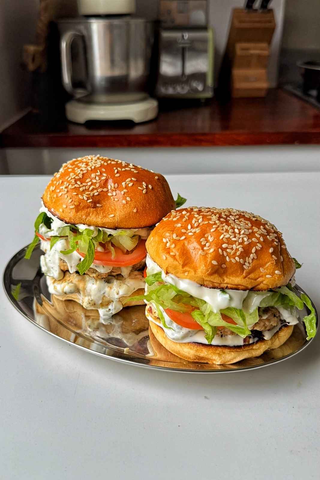 two greek chicken burgers on stainless steel tray.