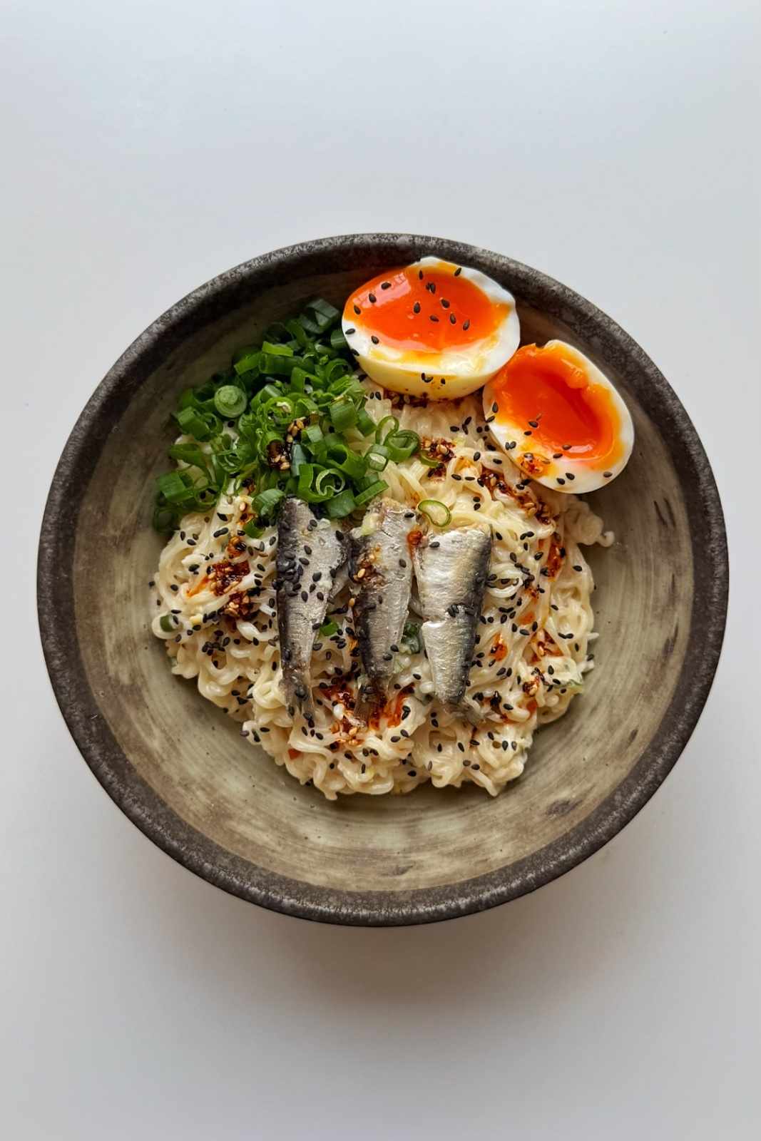 Sardine ramen in brown bowl with jammy eggs, scallions, and canned sardines.