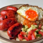 a plate of sausages, garlic fried rice, fried eggs, tomatoes, and cucumbers.