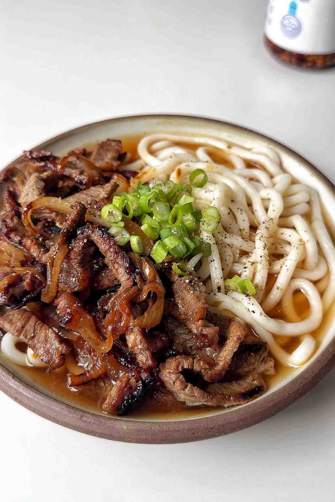 Brothy beef udon in a bowl topped with scallions.