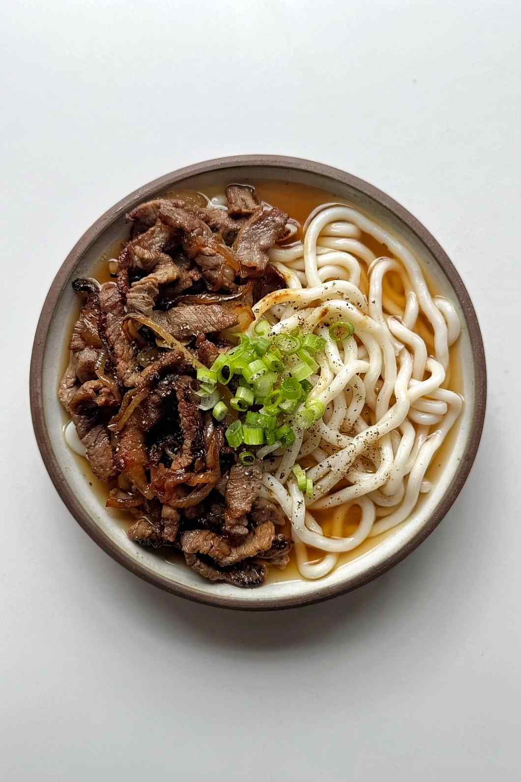 bowl of beef udon in broth topped with scallions