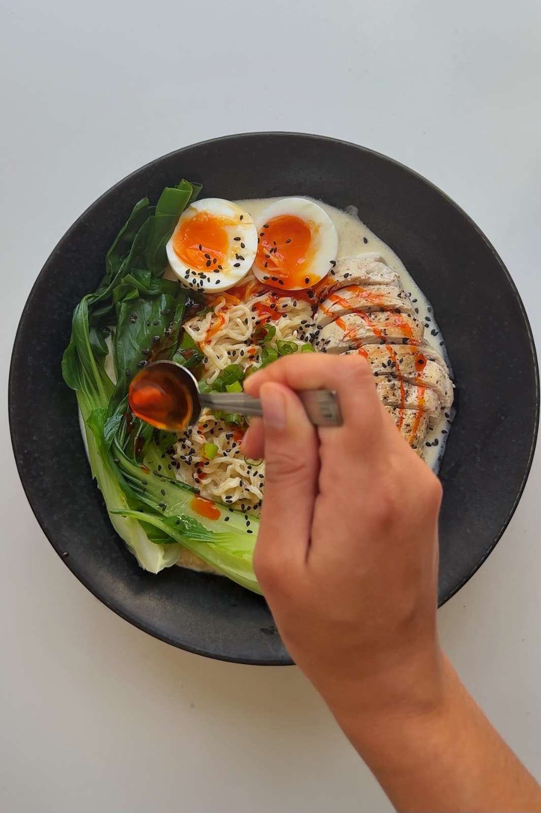 Garnishing chicken caesar ramen in a black bowl.