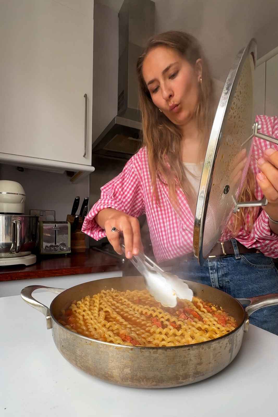 Emily Roz stirring chorizo pasta holding the lid.
