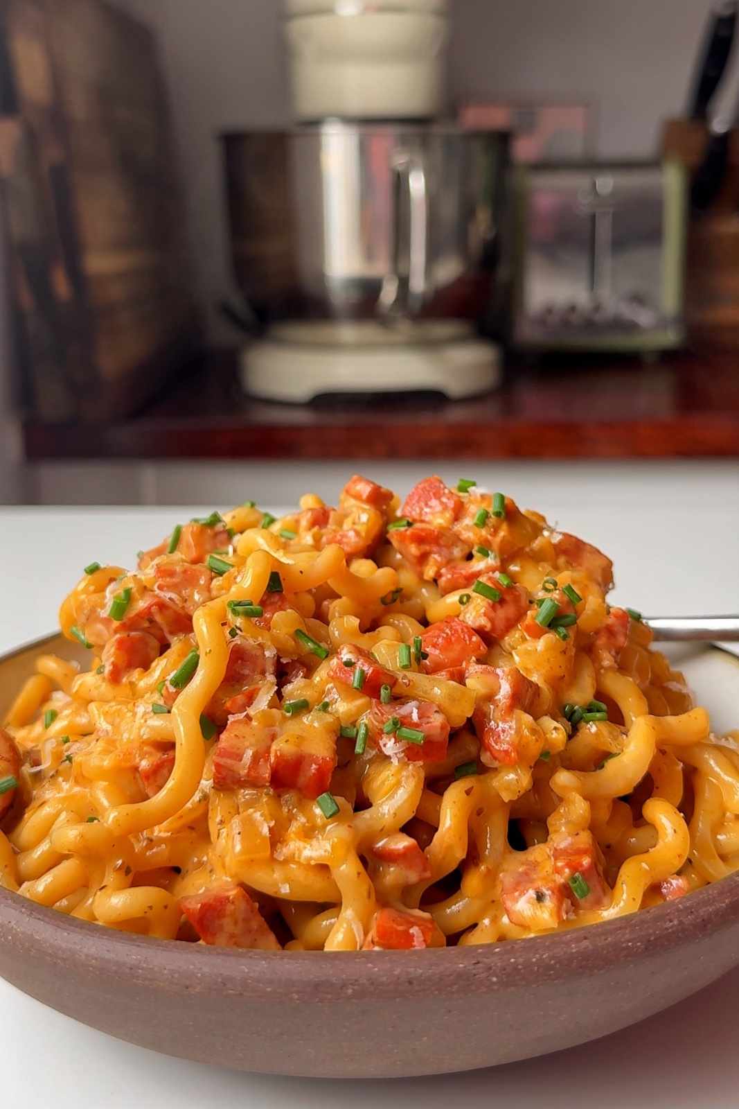 A bowl of chorizo pasta topped with grated parmesan and chopped chives.