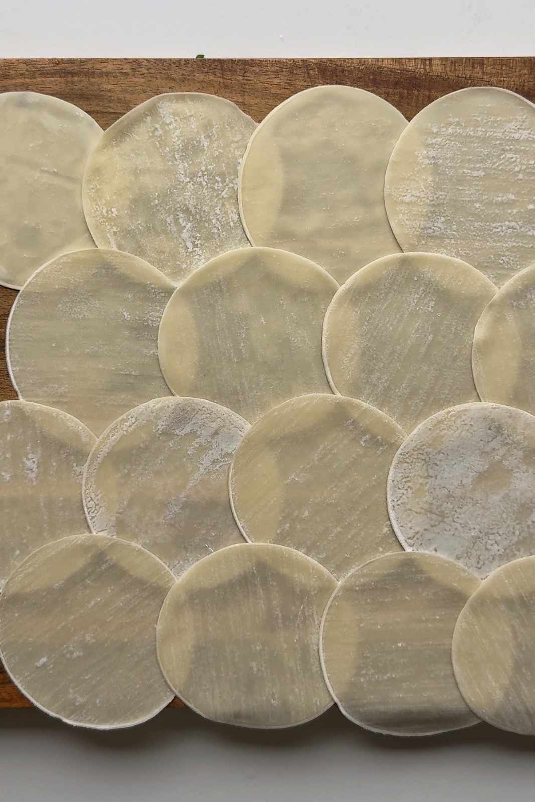 A layer of dumpling wrappers on a chopping board.