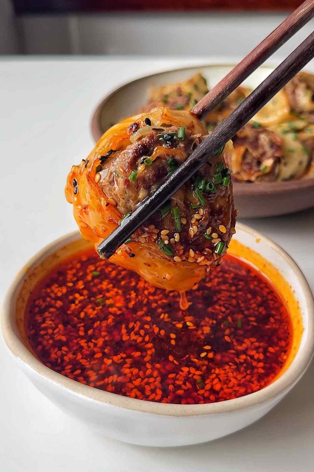 Dumpling wheel being dipped in chilli oil broth.