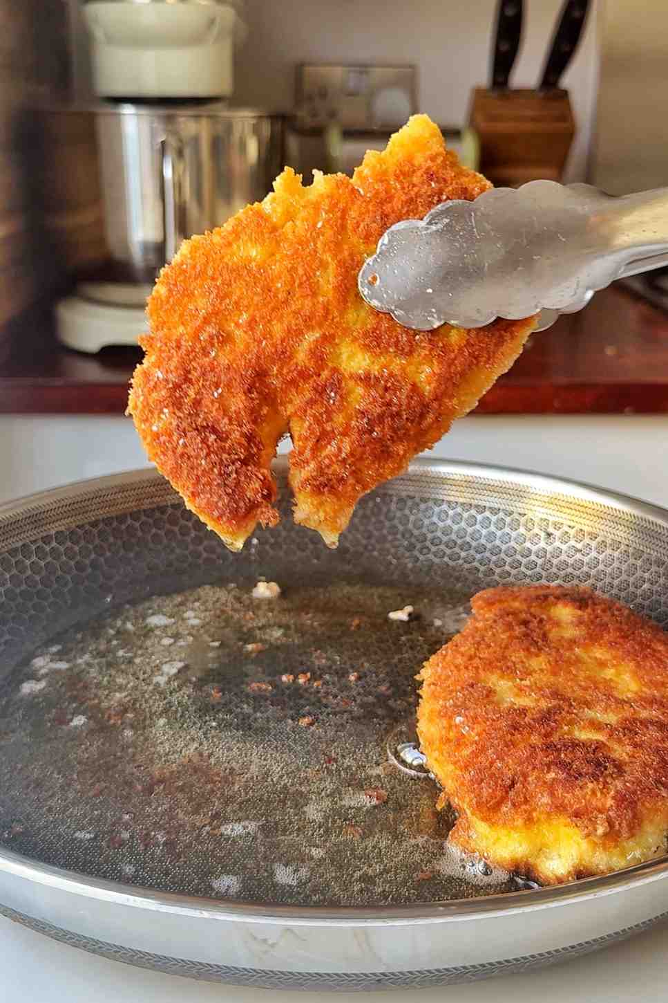 Fried chicken being held up with tongs.