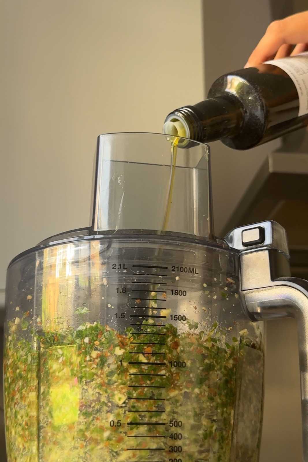 Pouring olive oil into blender to make pesto.