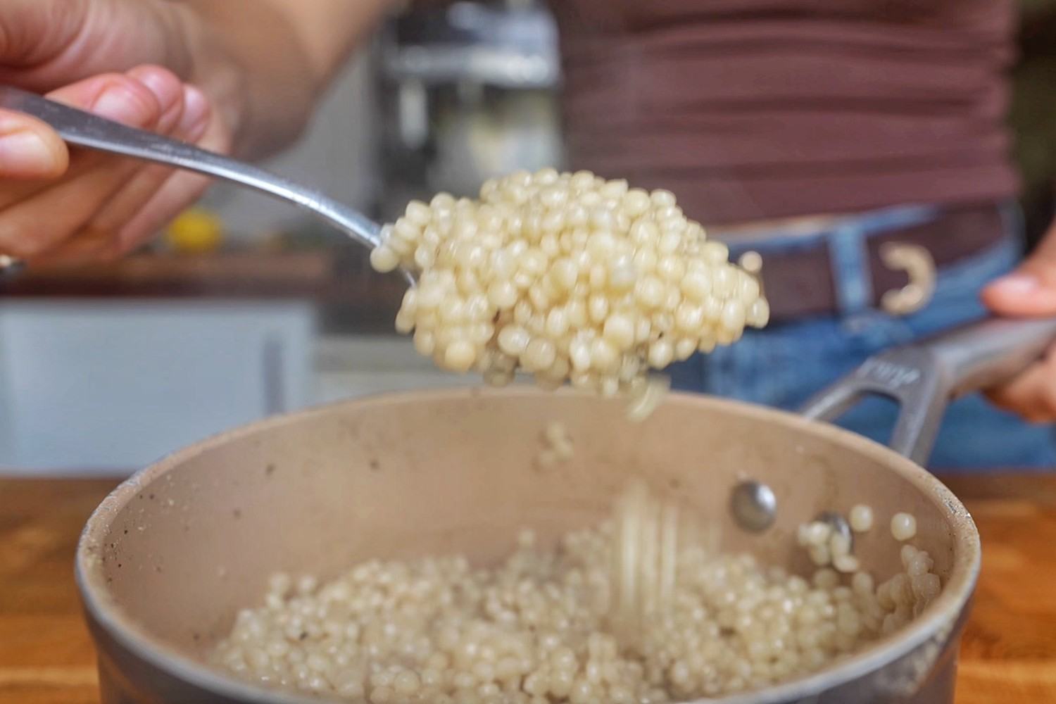 Spoonful of cooked pearl couscous lifted out of a saucepan.