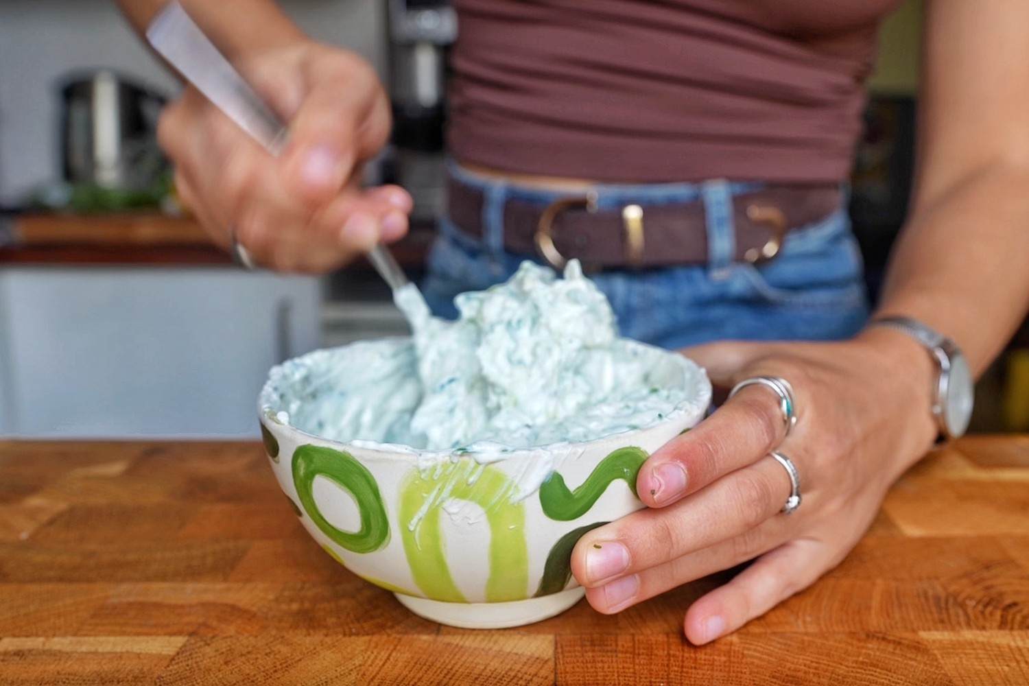 Emily mixing homemade tzatziki with a spoon in a green patterned ceramic bowl.