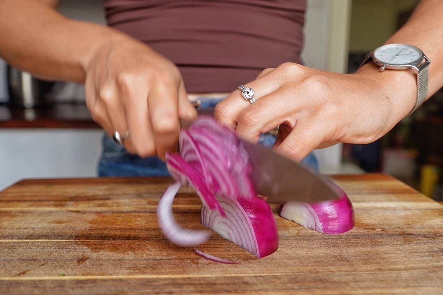 Emily thinly slicing a red onion on a wooden chopping board.