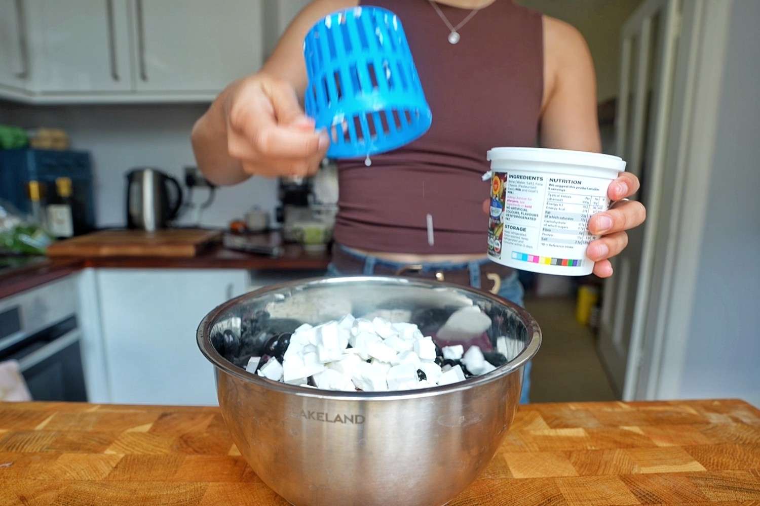 Adding cubed feta and black olives to a large steel mixing bowl.