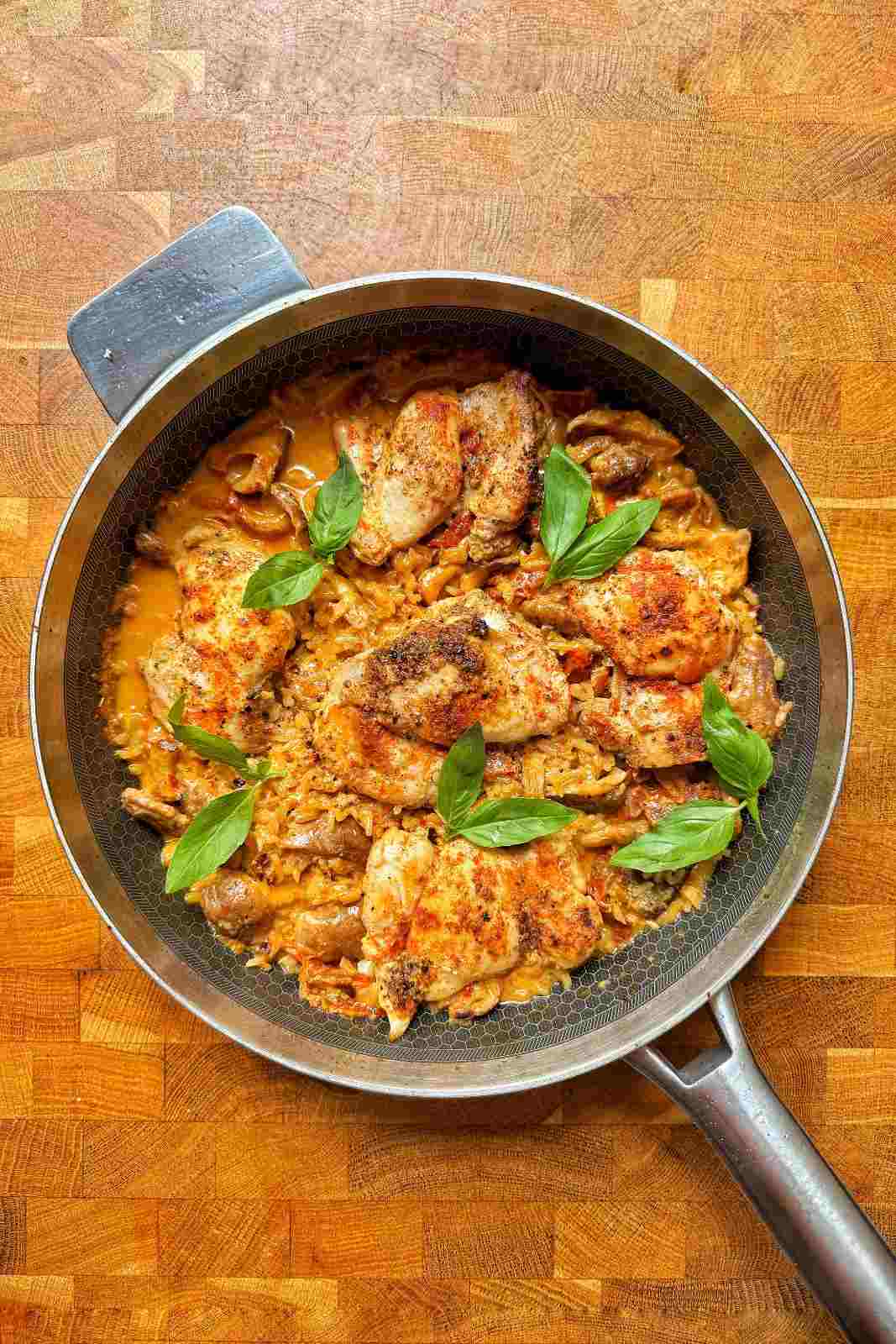 Overhead view of one pot marry me chicken and rice in a skillet, topped with seared chicken thighs and fresh basil.