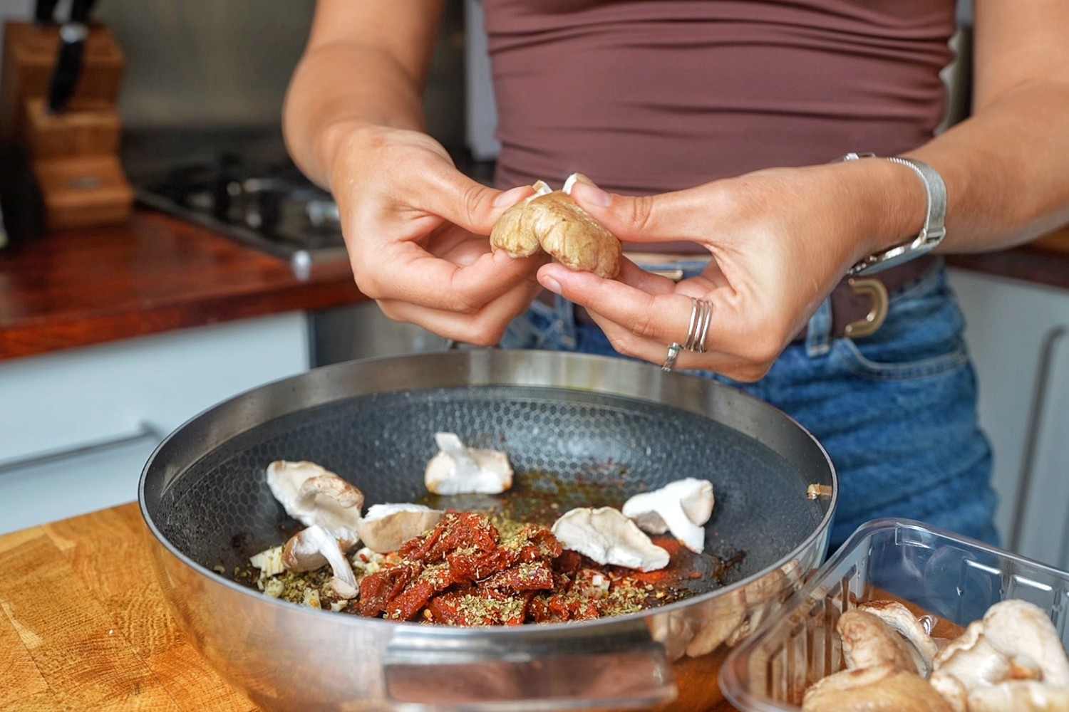 Emily adding torn mushrooms to a skillet with chopped garlic, sun-dried tomatoes, paprika and dried oregano.