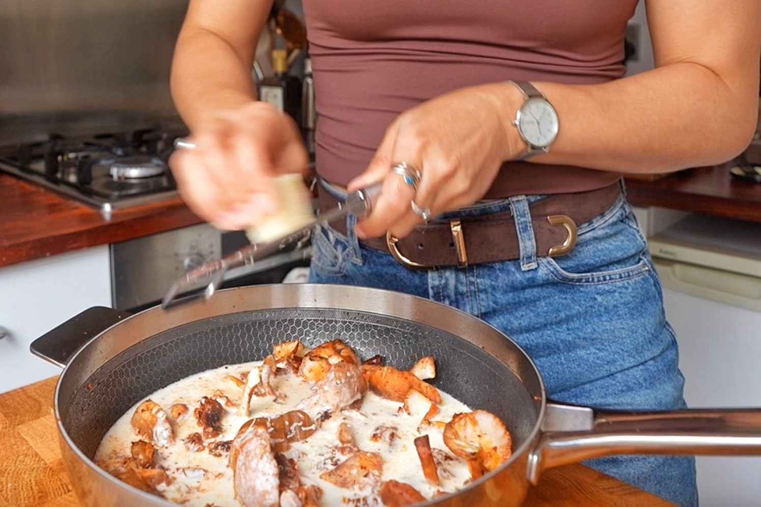 Emily grating Parmesan into a skillet of cream, mushrooms and sun-dried tomatoes.