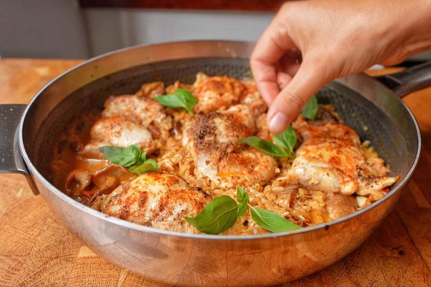 Hand scattering fresh basil leaves over cooked marry me chicken and rice in a skillet.