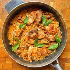 Overhead view of one pot marry me chicken and rice in a skillet, topped with seared chicken thighs and fresh basil.
