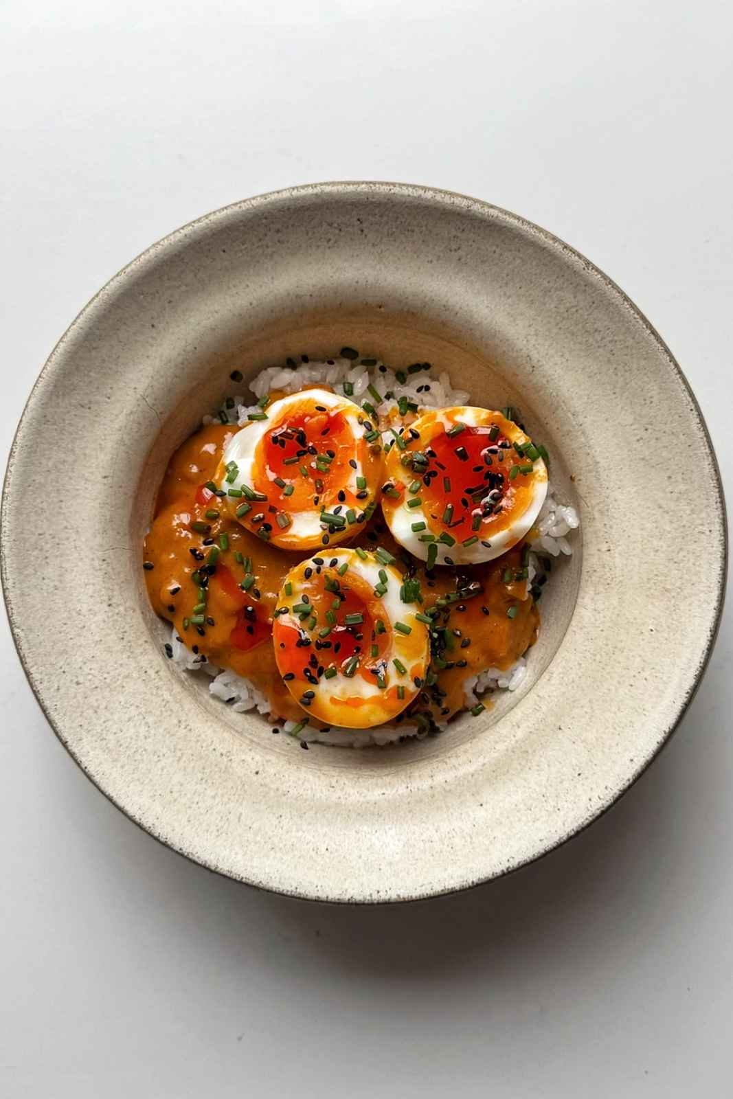 white bowl filled with rice and topped with peanut gochujang chili eggs.