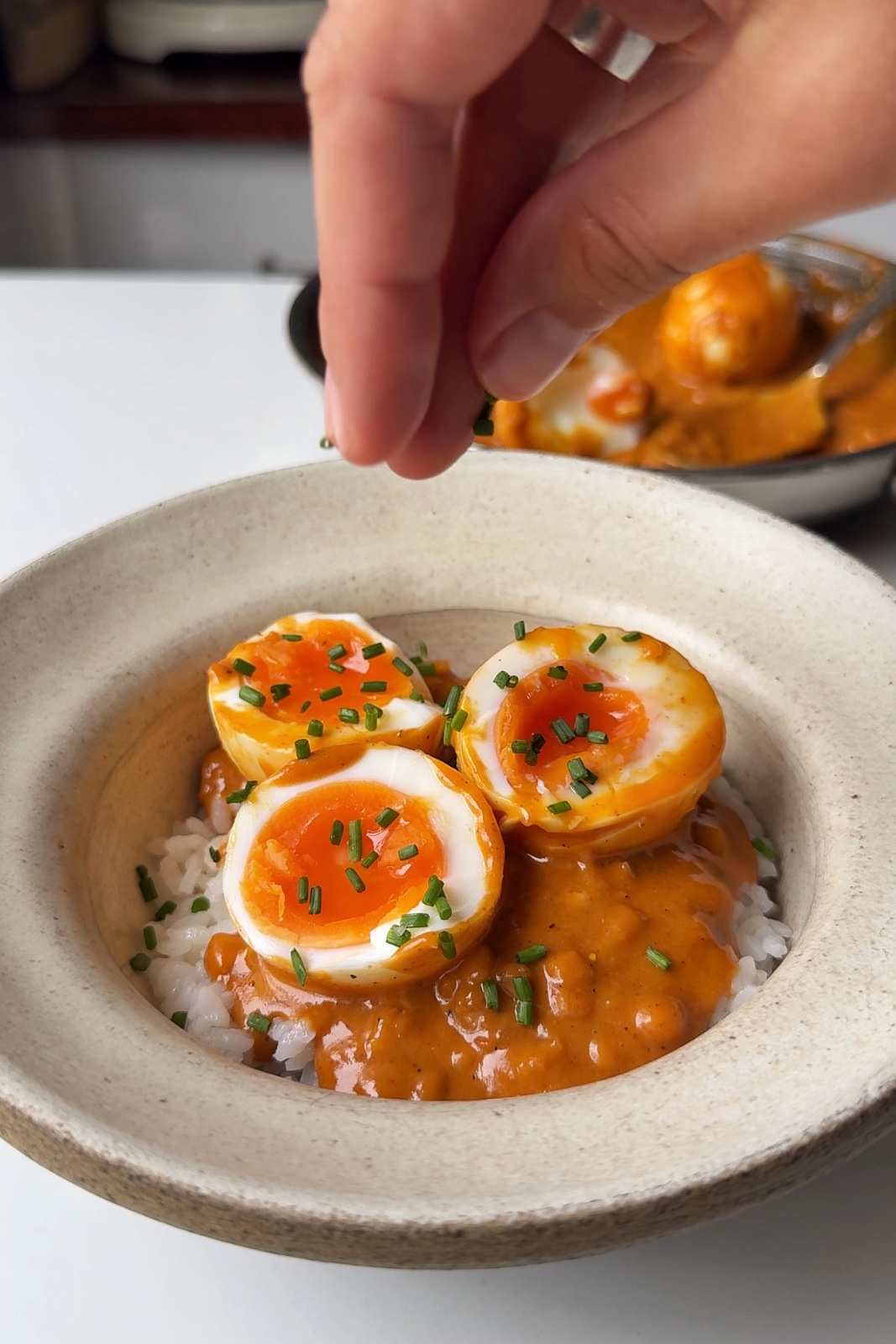 Garnishing the peanut gochujang chili eggs with chives and sesame seeds.