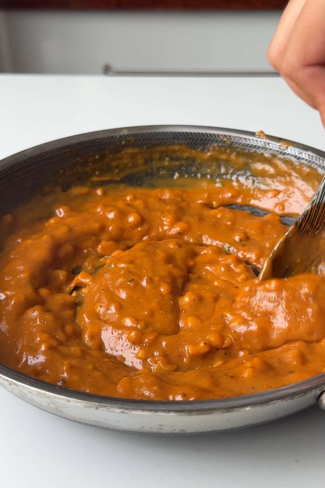 Stirring the gochujang peanut chili sauce with a wooden spoon in a skillet.