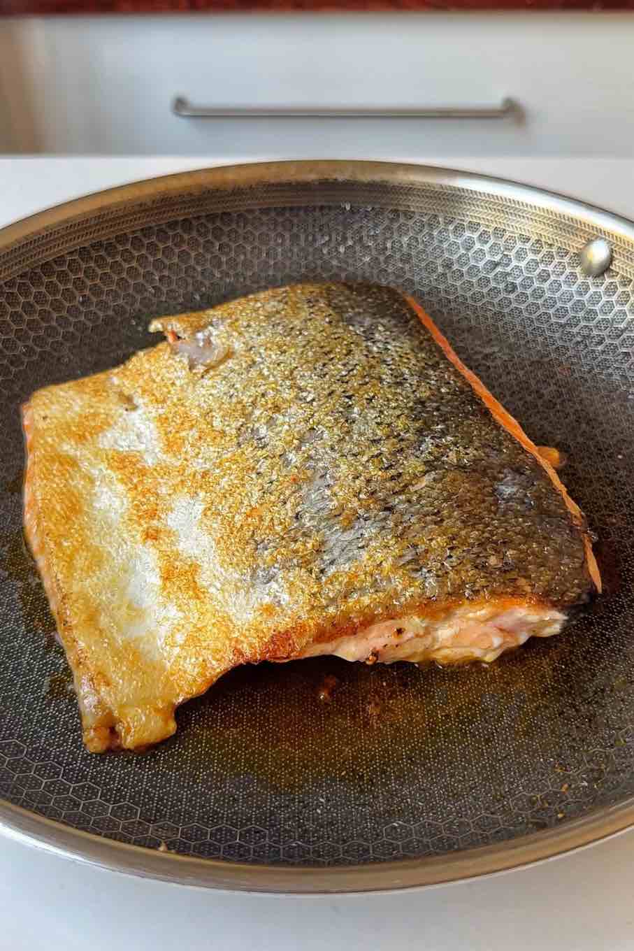 Frying side of salmon in a pan.