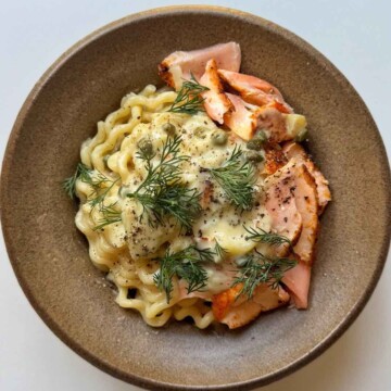 Salmon pasta in a brown bowl topped with capers and dill.
