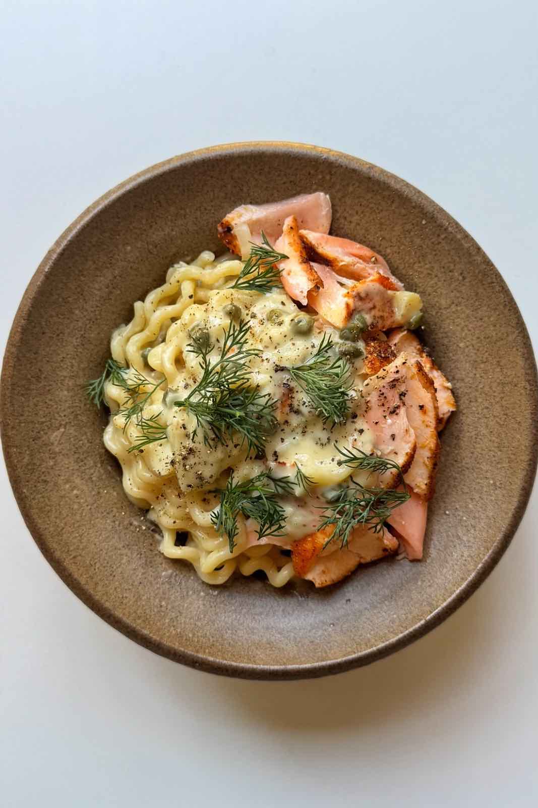 Salmon pasta in a brown bowl topped with capers and dill.