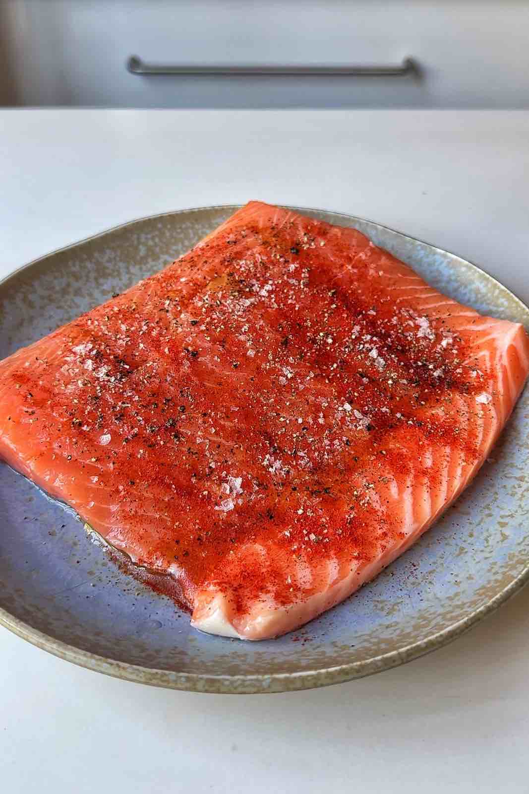 Seasoned side fillet of salmon on a blue plate.