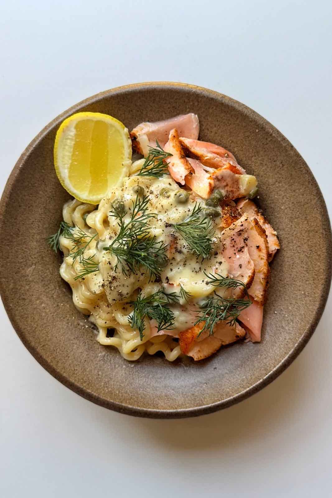 bowl of salmon pasta with lemon topped with dill and capers.