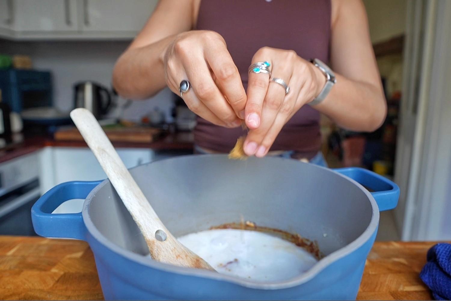 Emily crumbling a stock cube into a pot of coconut milk and peanut curry broth.