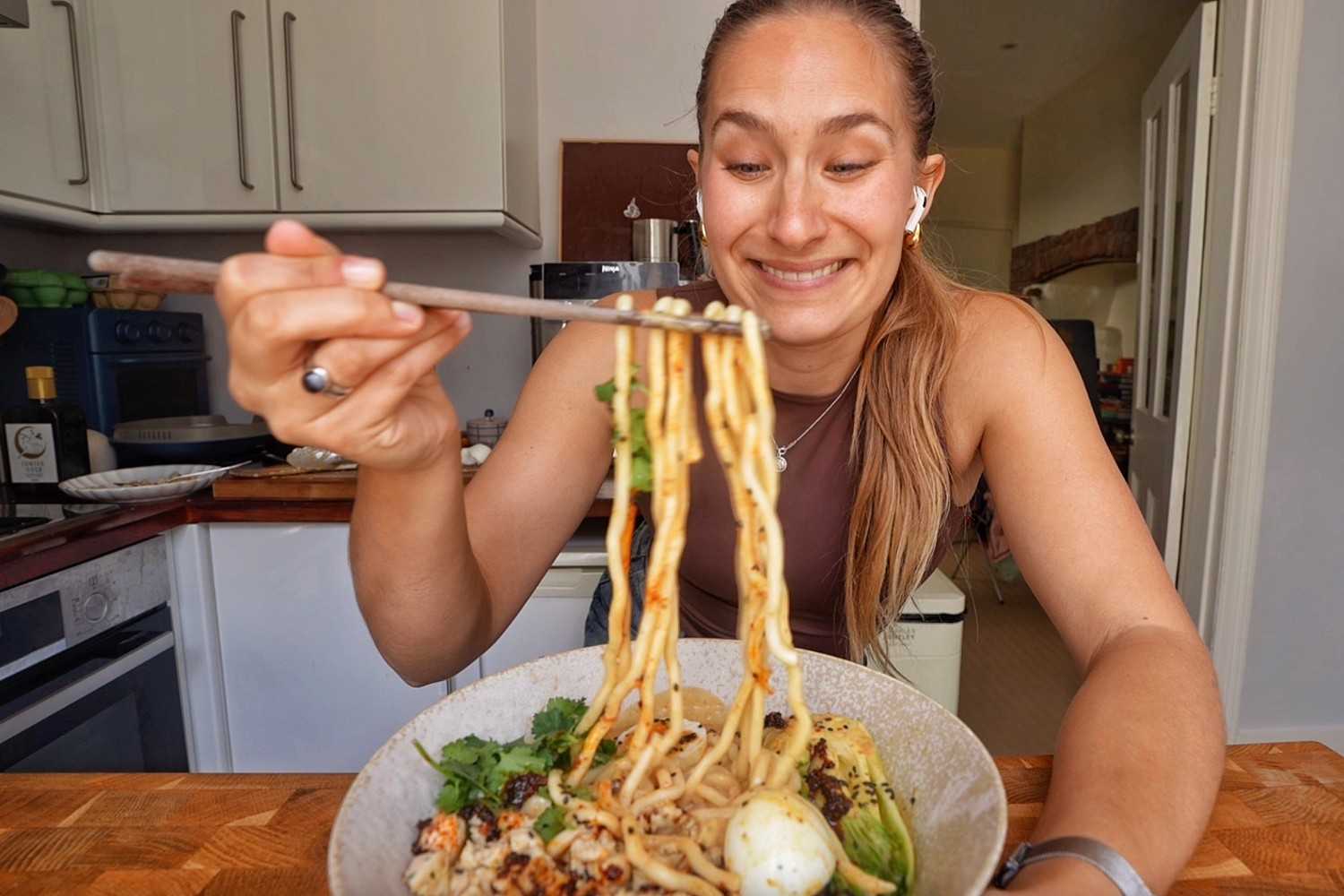 Emily lifting udon noodles out of a bowl of peanut sausage ramen with chopsticks.