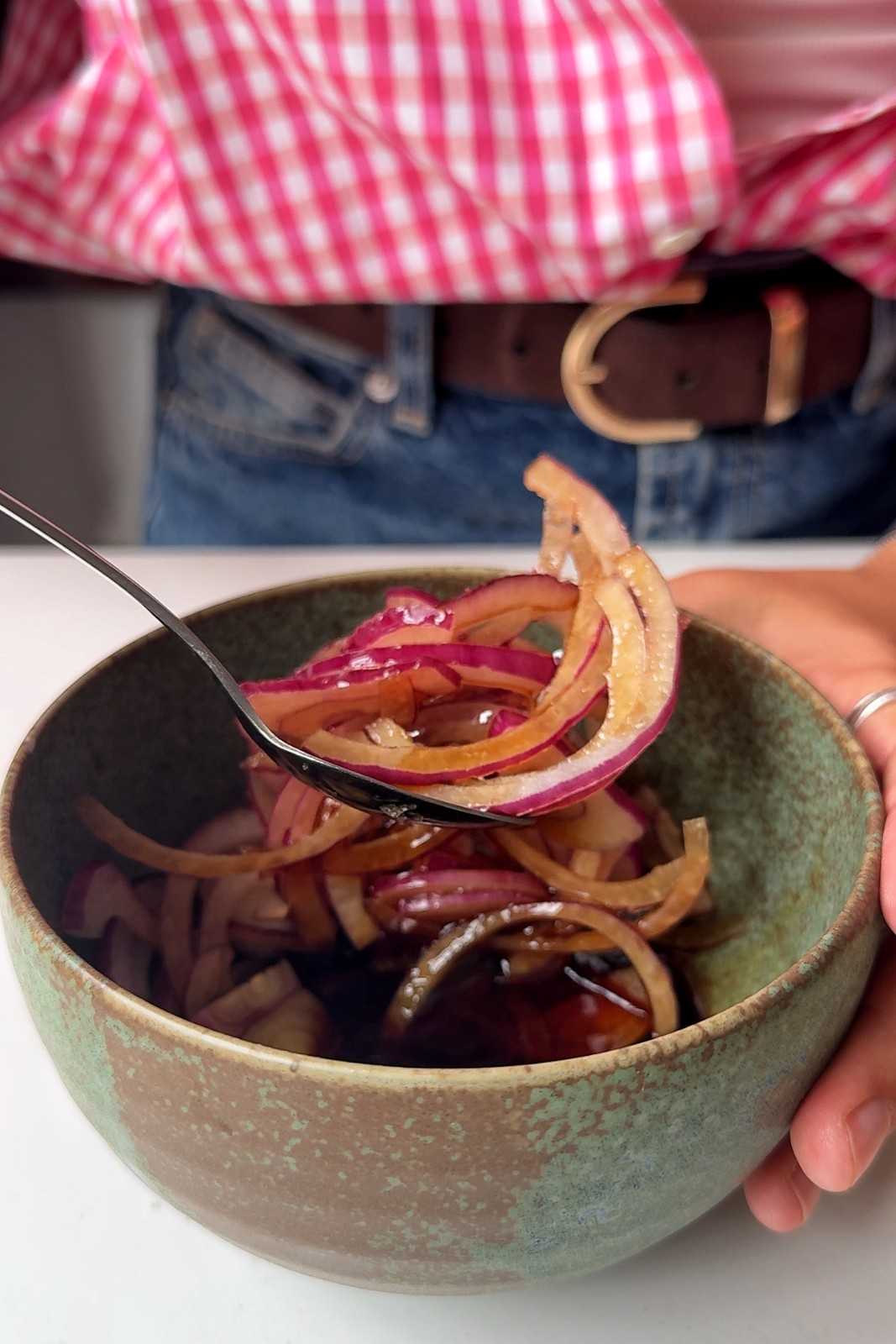 Quick pickled red onions turning bright pink in a green ceramic bowl.