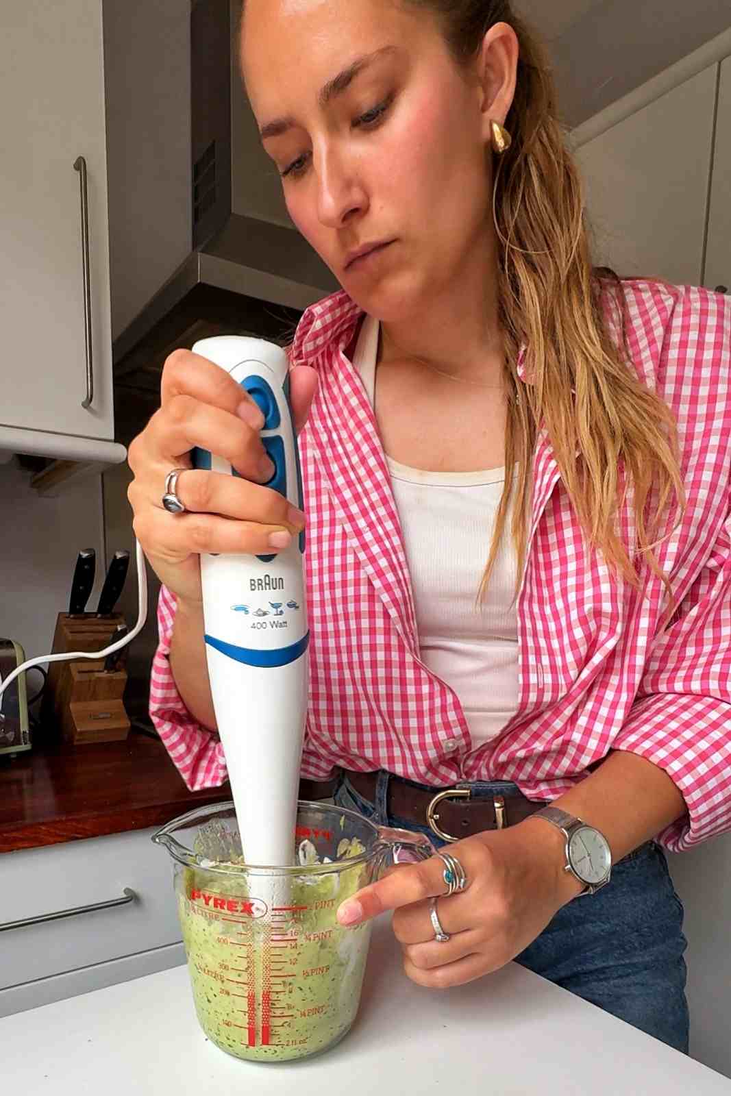 Blending bright green avocado sauce with a hand blender in a glass measuring jug.