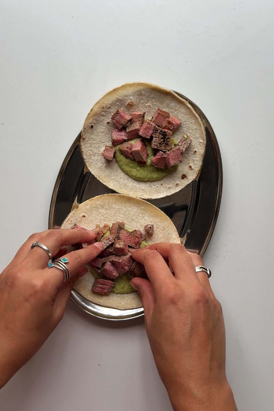 Emily assembling steak tacos by adding cubed steak on top of avocado sauce on warm tortillas.