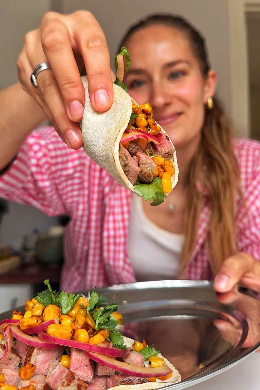 Emily holding a steak taco filled with charred corn, pickled red onion and cilantro.