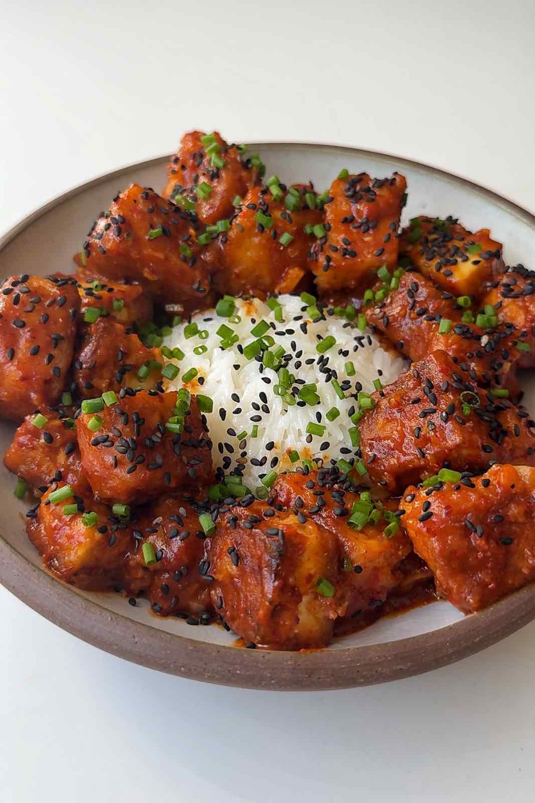 A bowl of sticky orange tofu topped with chives with rice.