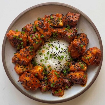 A bowl of sticky orange tofu topped with chives with rice.