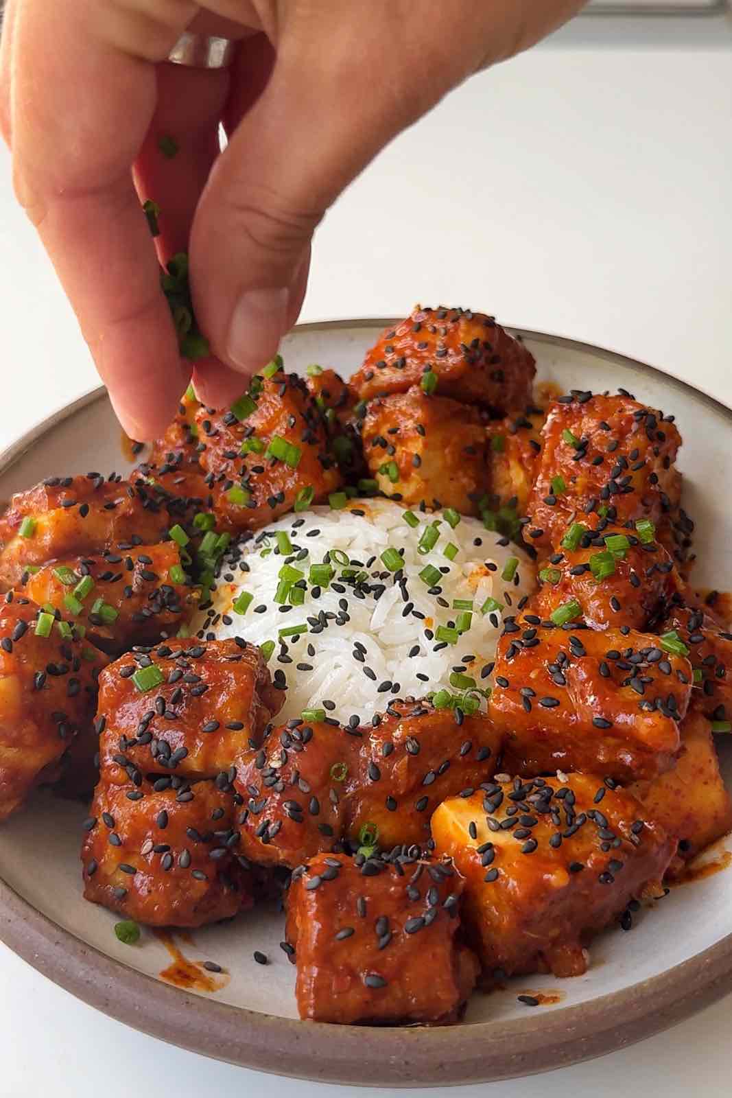 Dishing up sticky orange tofu topping with chives.
