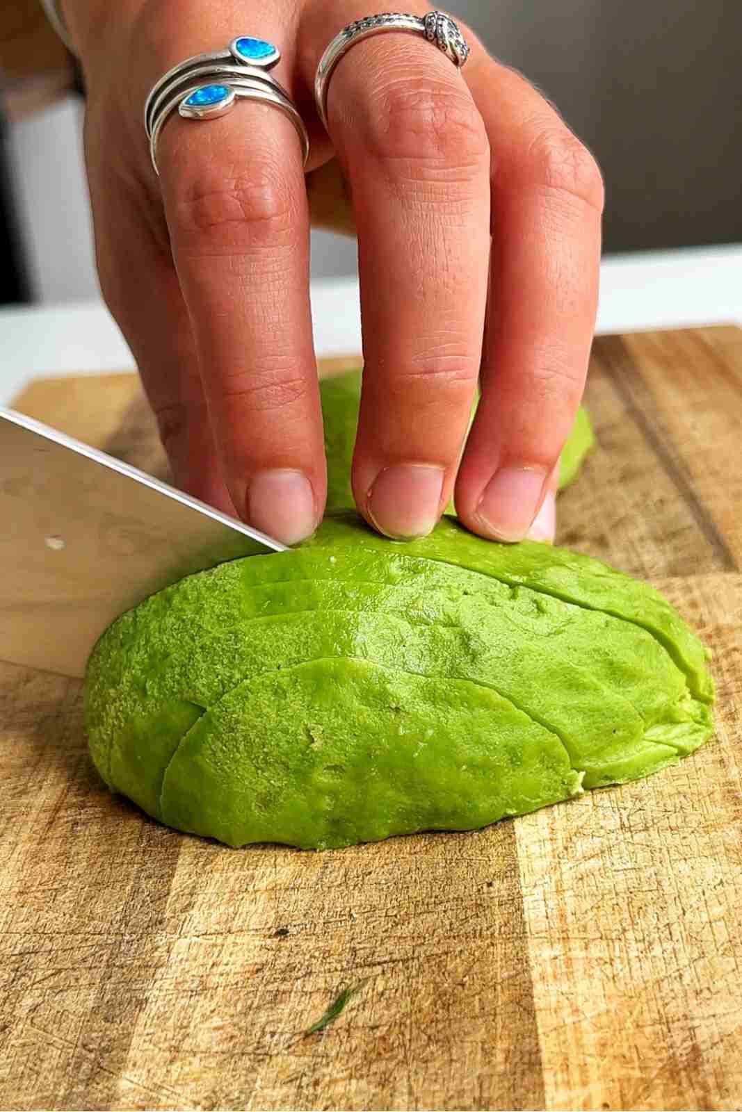 Slicing a peeled avocado half into thin slices on a wooden chopping board.