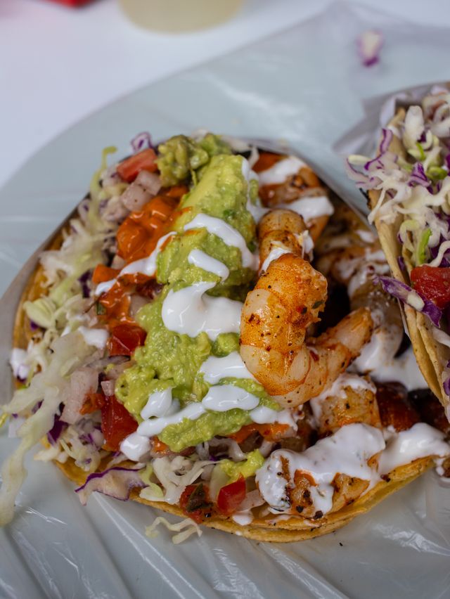 White Mexican crema drizzled over shrimp tacos with guacamole, pico de gallo and shredded cabbage on corn tortillas.