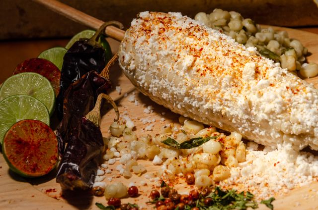 Crumbled cotija cheese and chile powder coating a cob of Mexican street corn with limes and dried chiles.