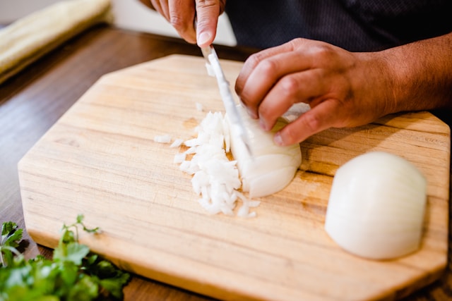 A white onion being thinly diced on a wooden chopping board.