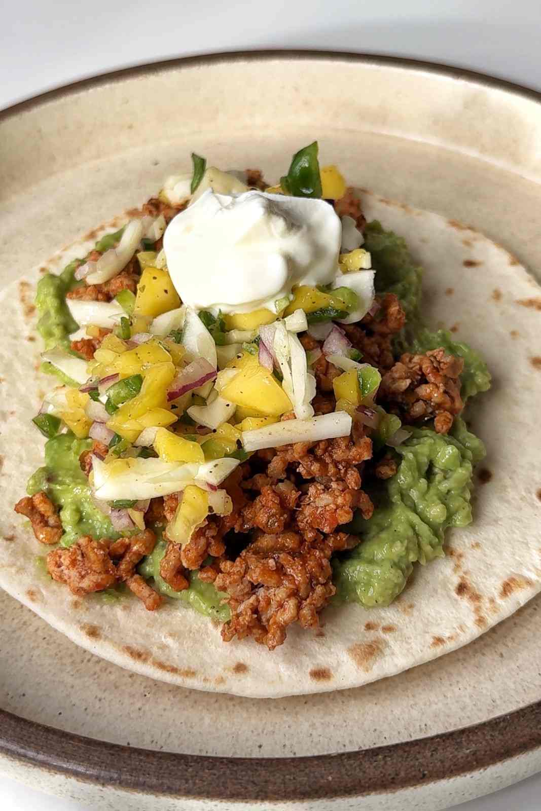 Shredded white cabbage in mango salsa on a ground pork taco with smashed avocado and sour cream.