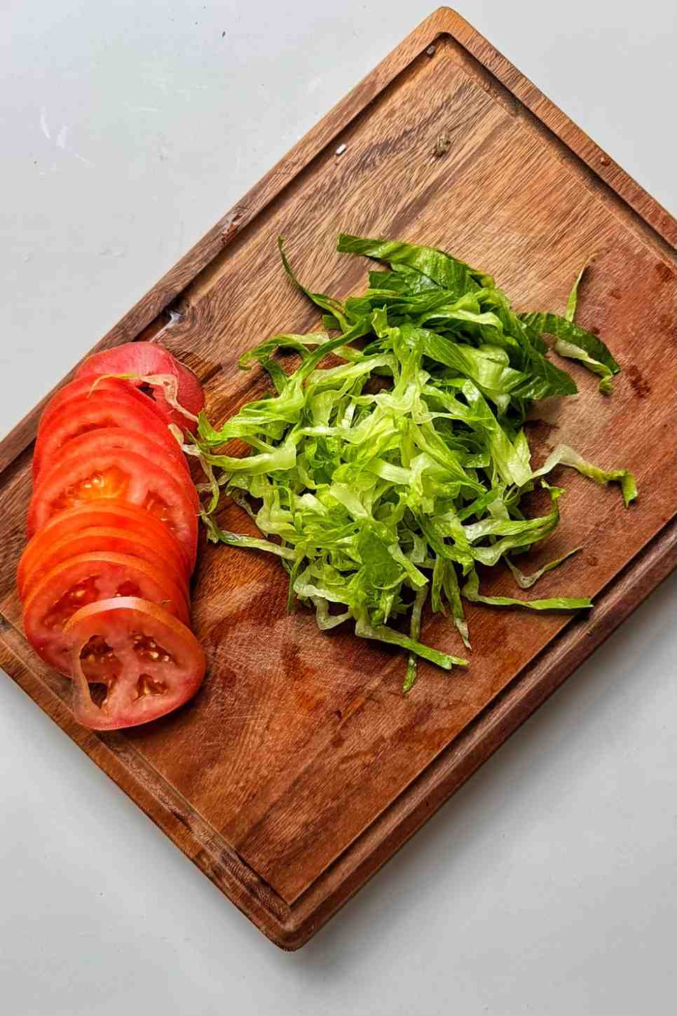 Shredded lettuce and sliced tomatoes on a wooden chopping board.